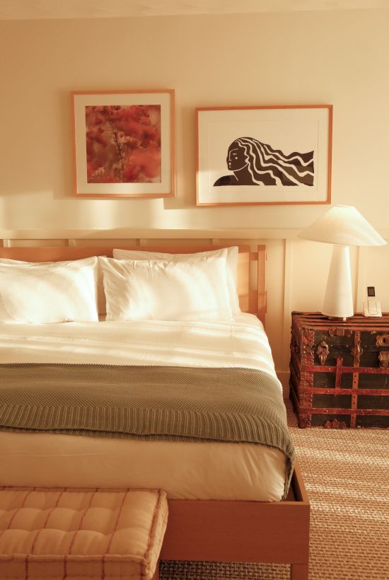 A cozy bedroom with a bed, green throw, artwork, side table, and lamp, creating a warm and inviting atmosphere.