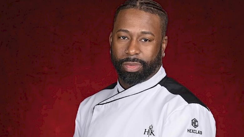 A person wearing a white chef's jacket with folded arms, standing against a red background.