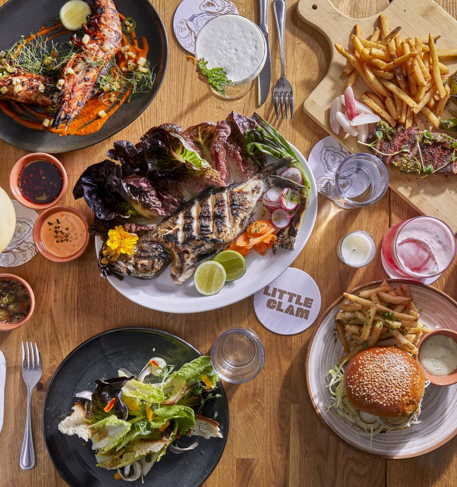 The image shows a variety of dishes, including steak, burger, fries, salad, and drinks, arranged on a wooden table.