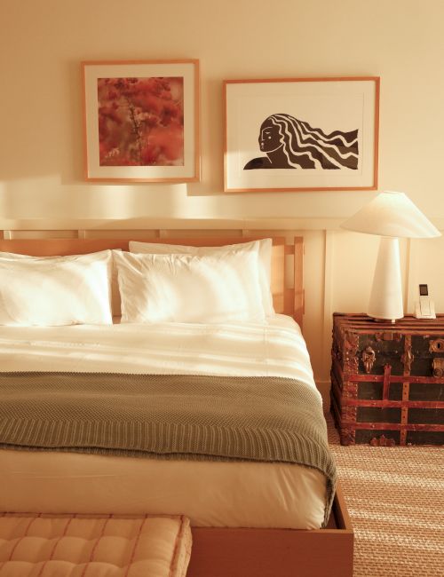 A cozy bedroom with a bed, green throw, artwork, side table, and lamp, creating a warm and inviting atmosphere.