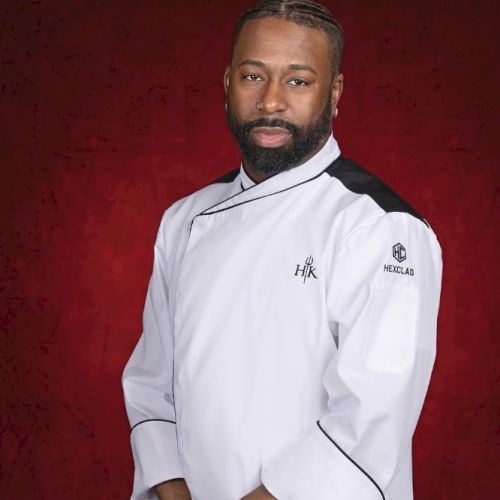 The image shows a person wearing a white chef's jacket with black accents, posed against a red background.
