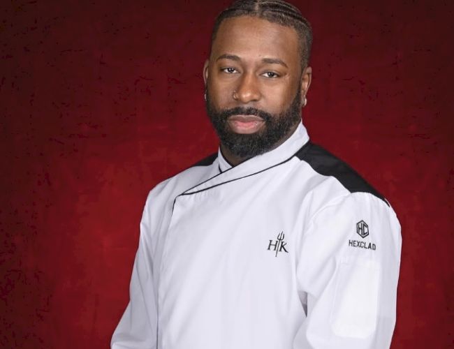 The image shows a person wearing a white chef's jacket with black accents, posed against a red background.