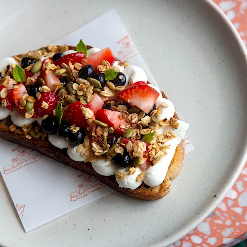 A fancy open-faced banana-bread toast topped with whipped cream, berries, granola, and mint&mdash;delicious, colorful bite-size dessert vibes.