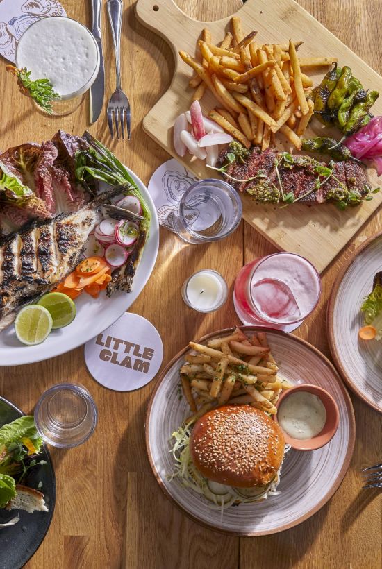 A table full of varied dishes: burgers, steaks, fries, salads, sauces, and drinks, all arranged for a shared, colorful feast.
